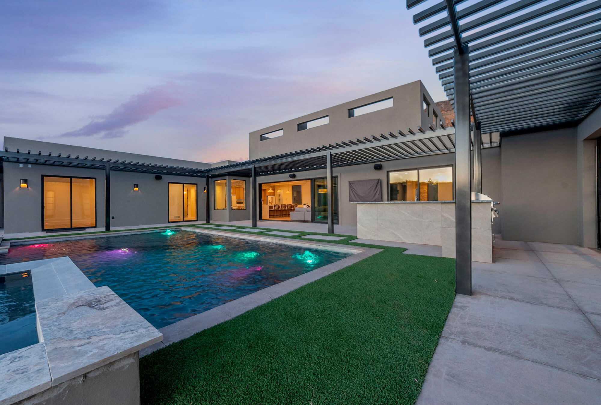 Modern home with a pool, colorful lights, and a spacious outdoor area at dusk, showcasing sleek architecture and landscaping.