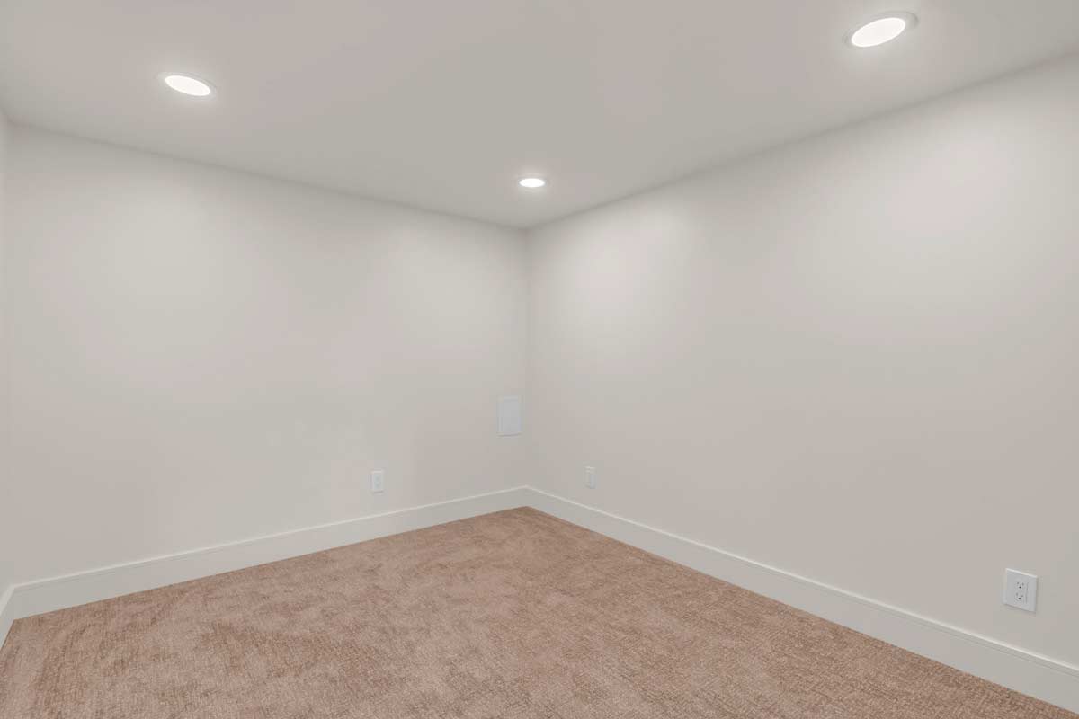 Minimalistic empty room with beige carpet, white walls, and three recessed ceiling lights. The space is bright and simple, giving an impression of a small, clean environment.